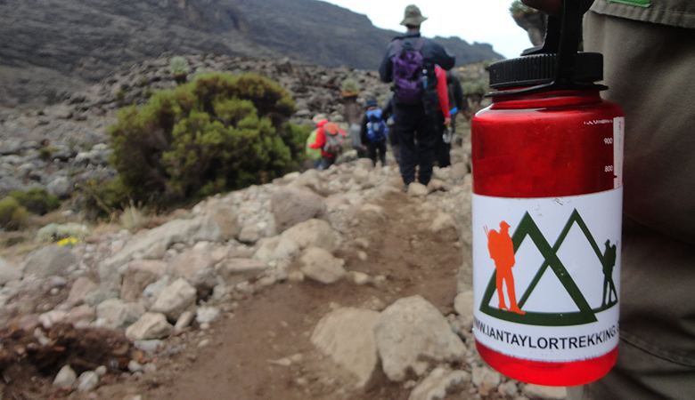 Water bottle on a rocky Kilimanjaro trail, with climbers walking ahead