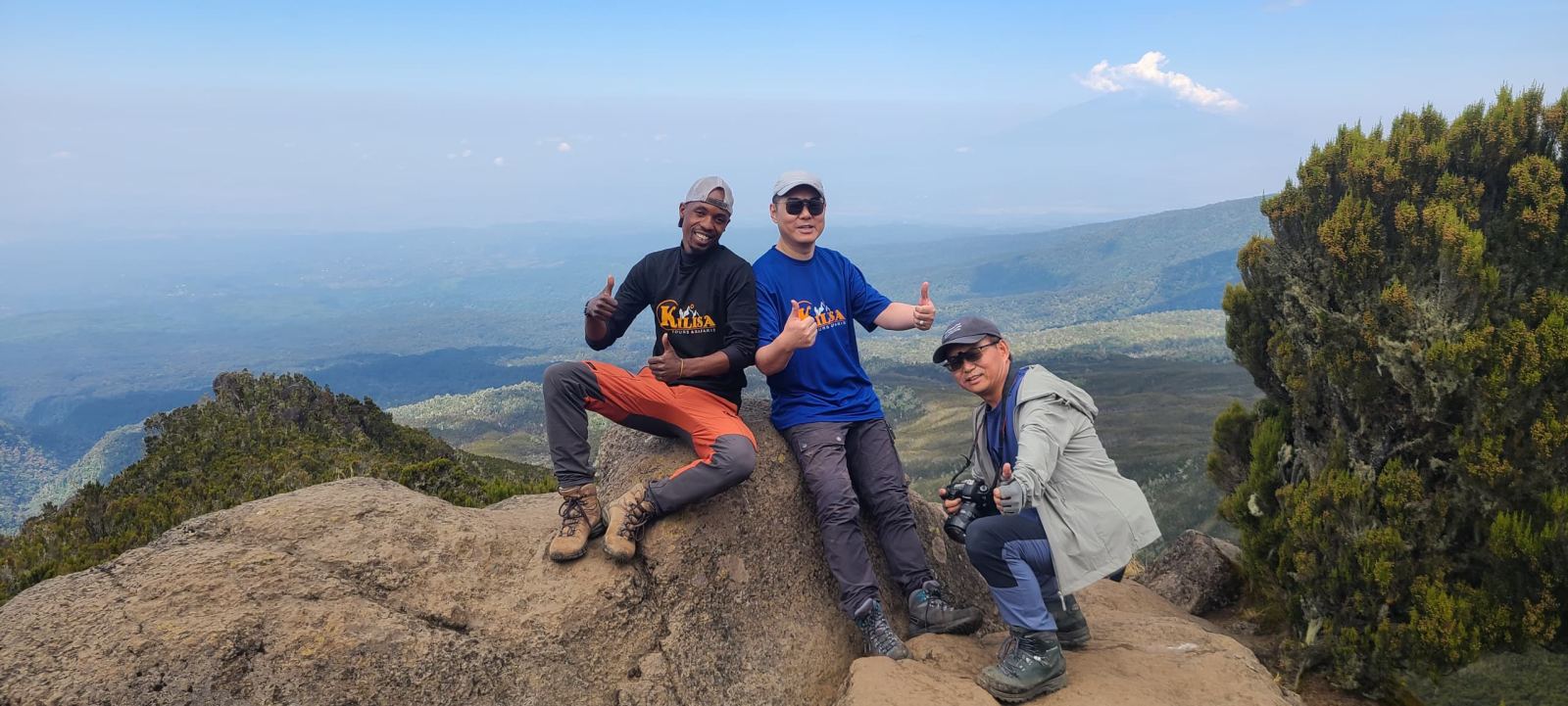Three trekkers sitting on a rock above the clouds on Kilimanjaro