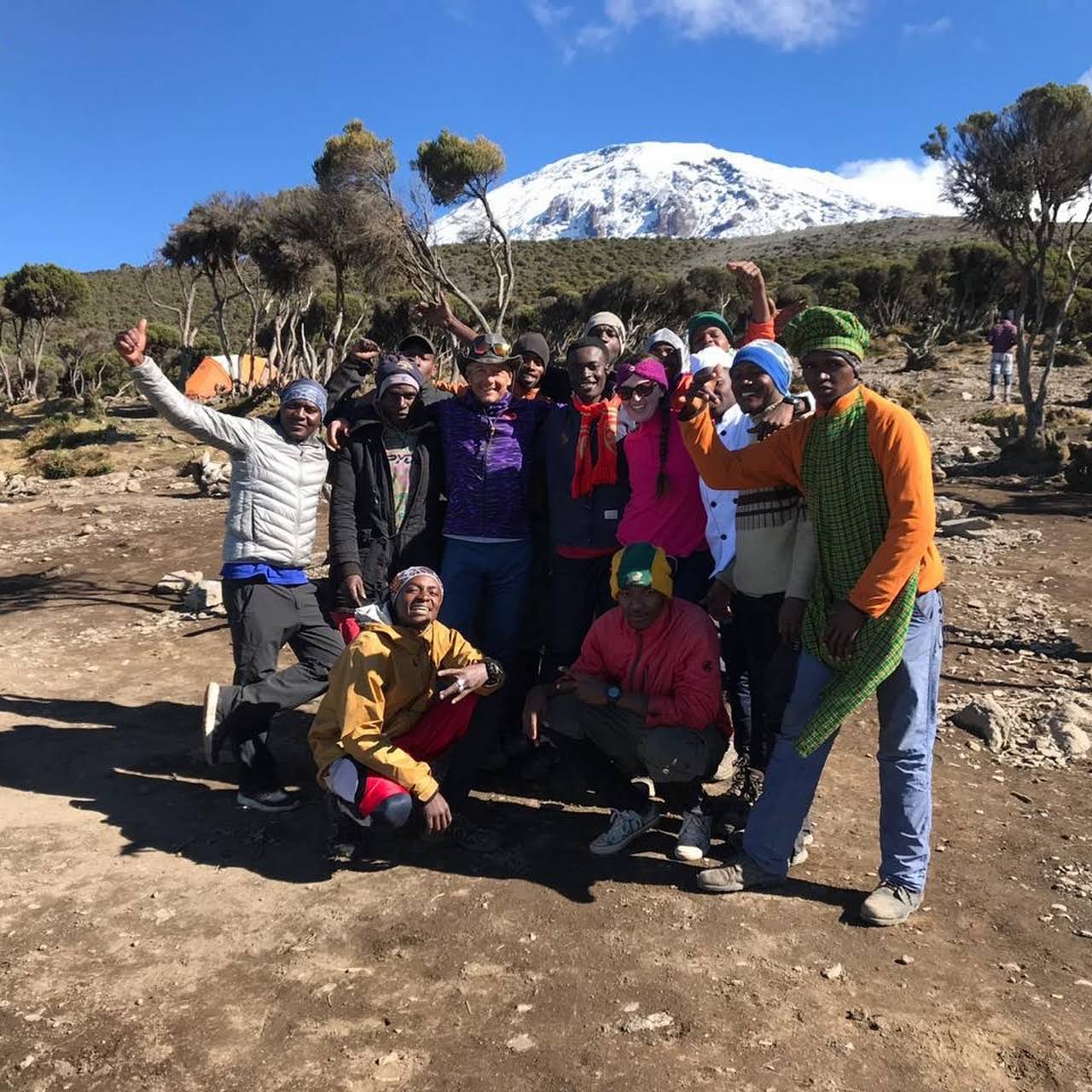 Group of climbers and guides posing at a camp with Kilimanjaro behind