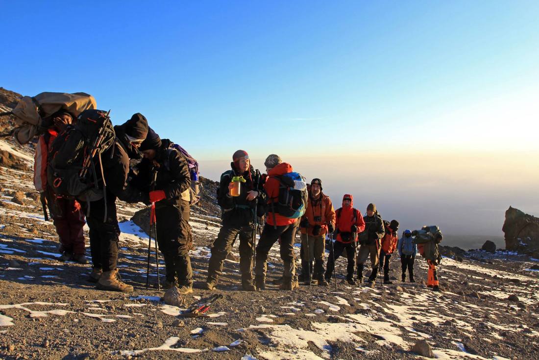 Line of climbers on a stony slope of Kilimanjaro at sunrise