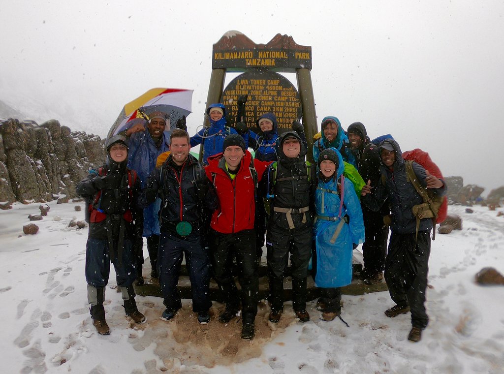 Group of climbers in rain gear at a camp sign on a snowy day on Kilimanjaro