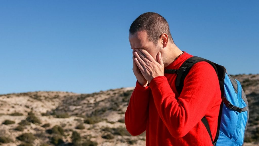 Hiker holding his face in his hands on a mountain trail