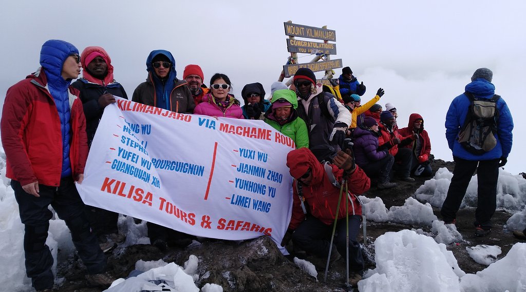 Climbers holding a Kilisa Tours banner in the snow on the Machame route