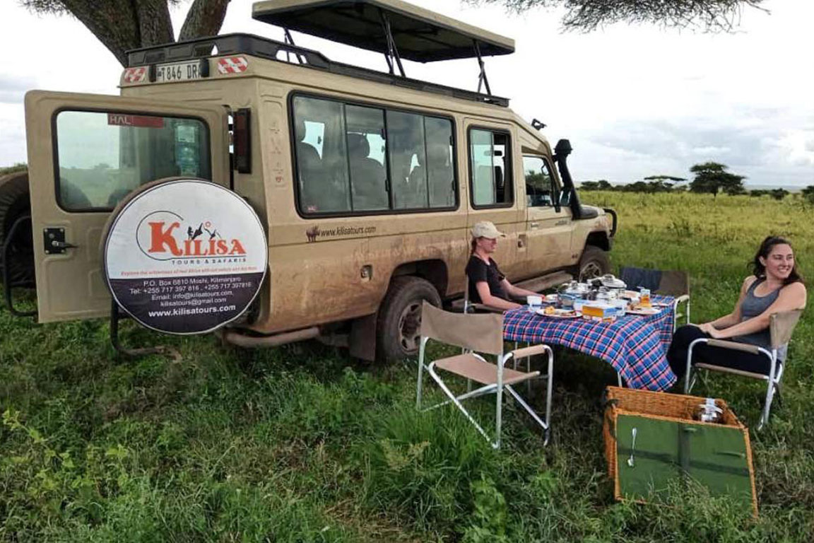 Kilisa Tours safari vehicle with a picnic table set up beside it on the grass