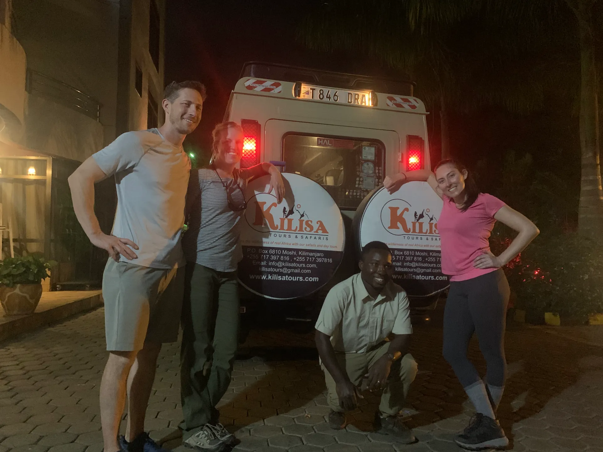 Guests and driver posing at night behind a Kilisa Tours safari vehicle