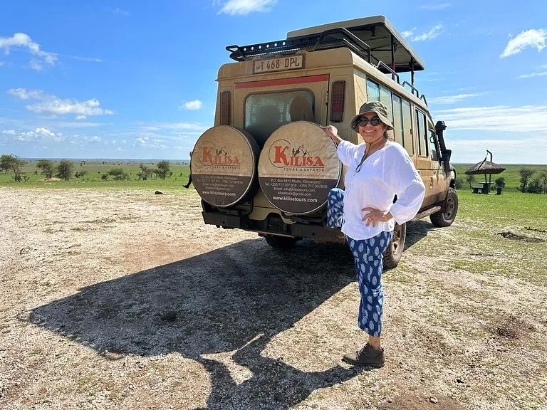 Guest posing beside a Kilisa Tours safari Land Cruiser on the open plains of Tanzania
