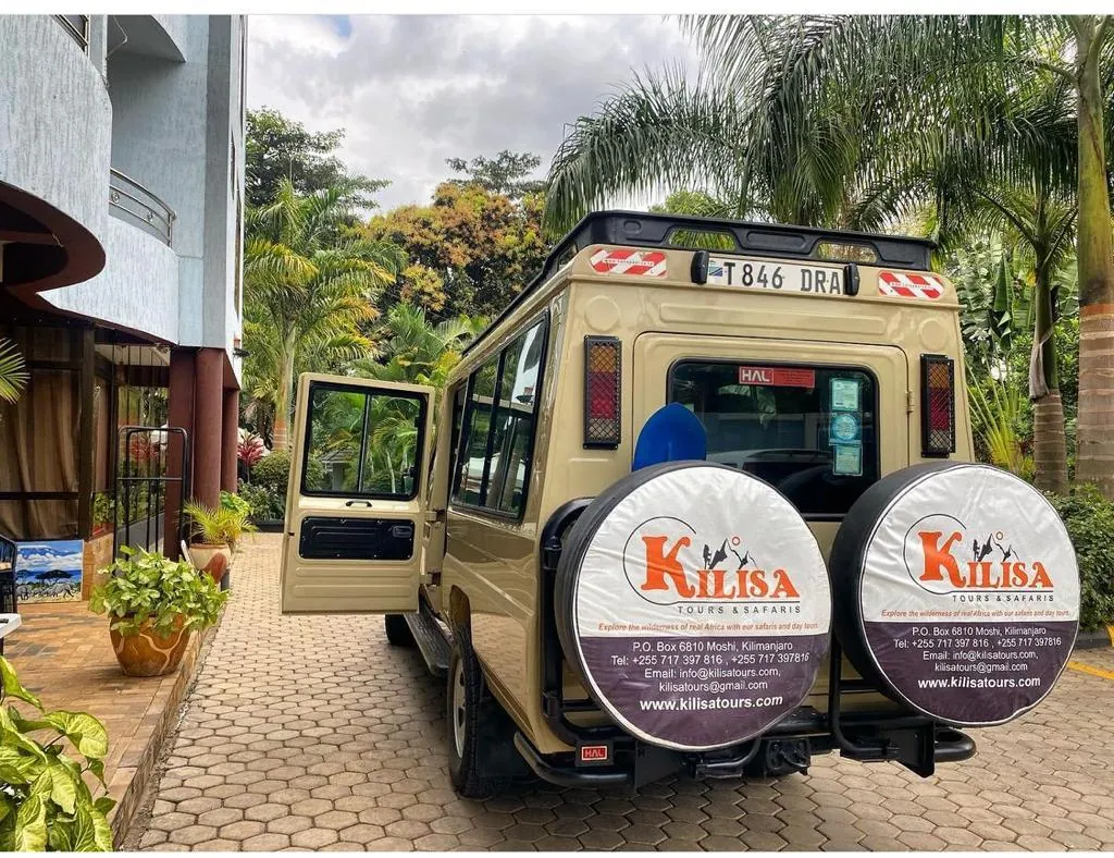 Kilisa Tours safari Land Cruiser with its doors open at a hotel entrance, ready for pickup