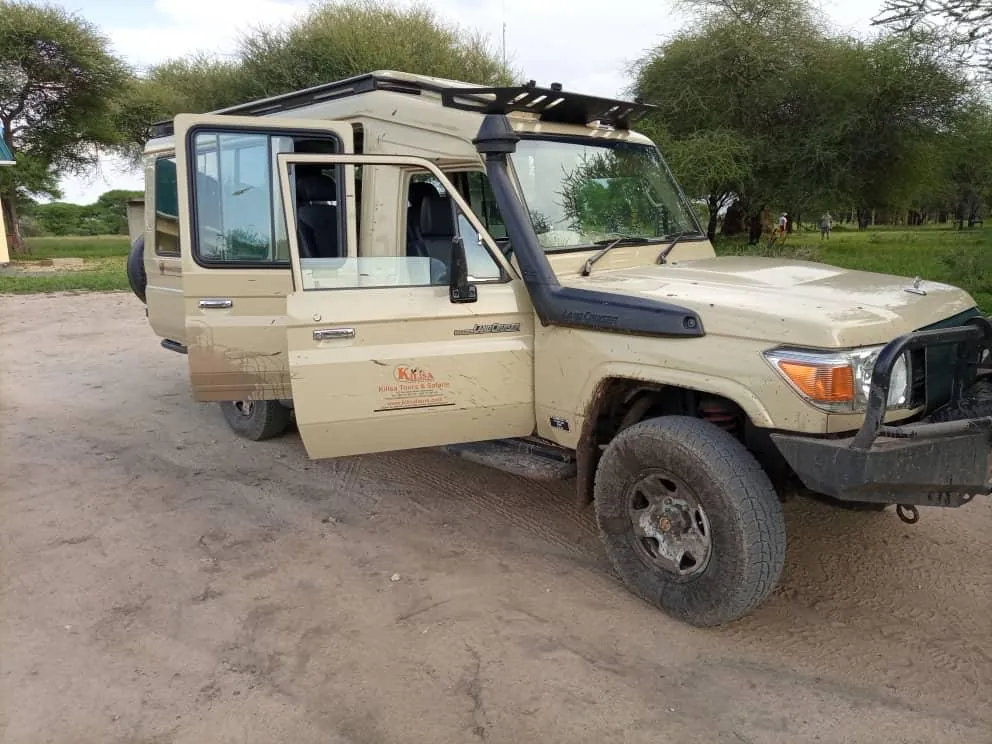 Kilisa Tours safari Land Cruiser with a pop-up roof parked under acacia trees