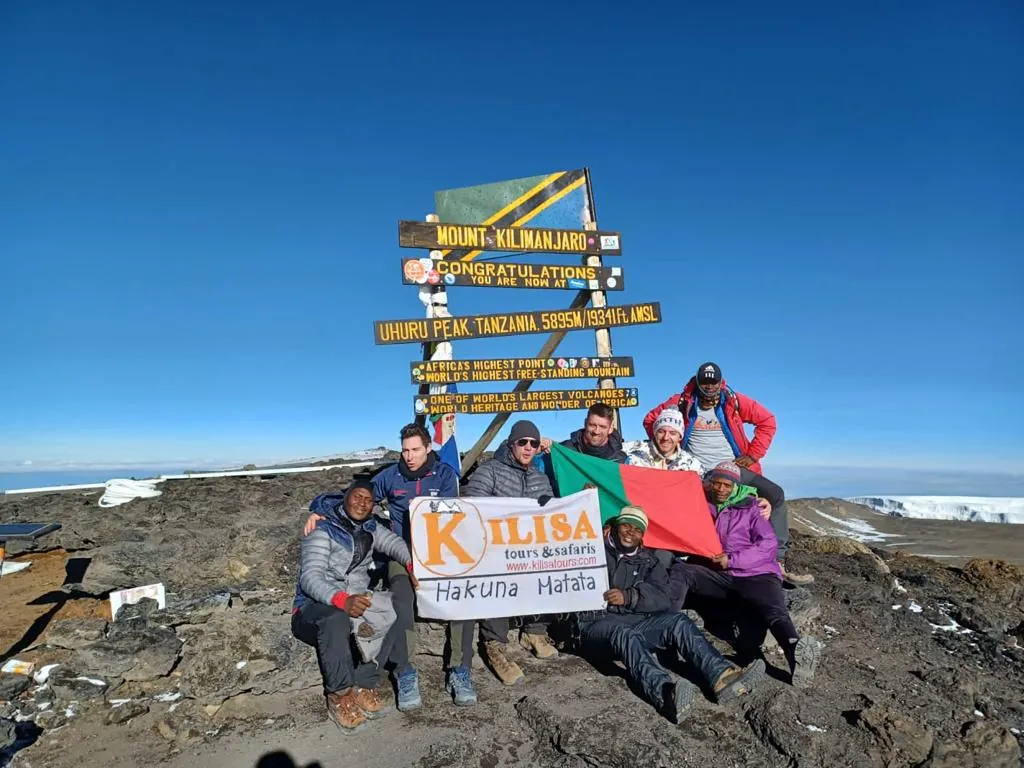 Group of climbers celebrating with a Kilisa Tours banner at the Uhuru Peak sign, 5,895 m, Mount Kilimanjaro
